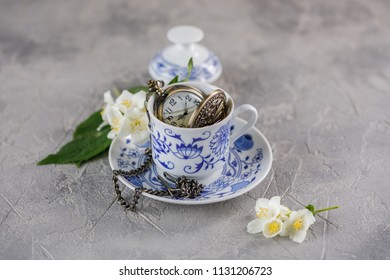 A ceramic cup of green tea with jasmine and a beautiful clock on a chain inside.
