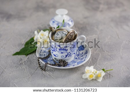 A ceramic cup of green tea with jasmine and a beautiful clock on a chain inside.