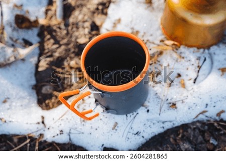 A ceramic cup that features an orangecolored handle is currently resting quietly in a patch of snow, contrasting the vibrant color of the handle with the white, cold snow surrounding it