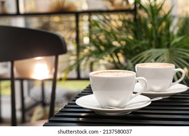 Ceramic cups of aromatic coffee with foam on wooden table in cafe