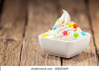 Ceramic Dish Of Decorative Twirled Vanilla Ice Cream Topped With Colorful Candy And Sprinkles For A Kids Birthday Party On An Old Wooden Table With Copyspace For Your Invitation Or Greeting