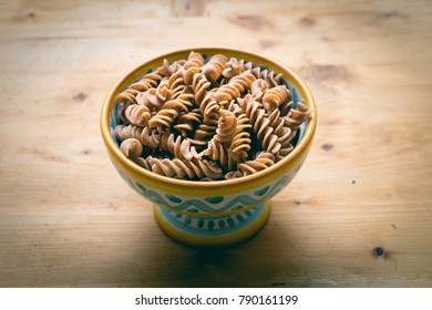 Ceramic dish filled with raw wholemeal fusilli pasta on a light wooden table - Shutterstock ID 790161199