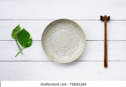 ceramic dish (plate) and chopsticks on white wooden table.Flat lay - Powered by Shutterstock