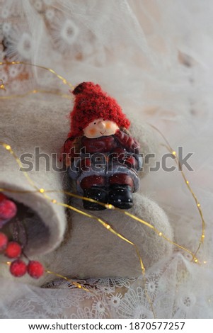 Ceramic doll in a warm red hat. Winter felt boots for the kid in New Year decorations. Good Mood During The Winter Holidays. Magic time for fulfilling your wishes. Merry Christmas