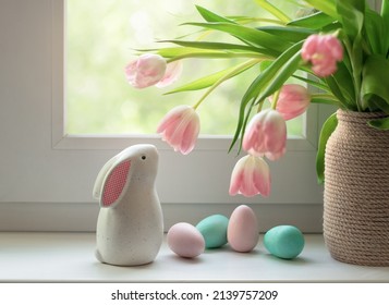 Ceramic Easter bunny, colorful dyed eggs and tulip flowers on windowsill. Decorations for Easter celebration at home. Selective focus.