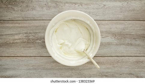 A Ceramic Ivory Mixing Bowl Of Cream Soft Cheese, Mixed With A Wood Spoon On Weathered Boards.