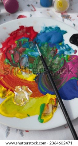 A ceramic palette with splashes of bright paint colors and a small brush on it.