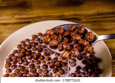 Ceramic plate with chocolate cereal balls in milk on rustic wooden table