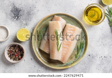 Ceramic plate with fresh cod fish, rosemary, lime, salt and olive oil on gray table. Mediterranean cuisine. copy space