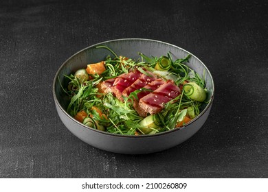 ceramic plate and salad with tuna fish, cucumber, green arugula and orange slices on a dark gray background side view