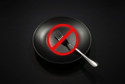 A Ceramic Plate With Silver Fork Together Isolated On Dark Background Close-up View, Food Concept Photography, No Eating Or No Food Sign On Centre Of The Image, Conceptual Image