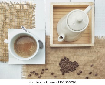 Ceramic set of hot coffee and teapot with coffee beans on burlap sack with white wooden tabletop in vintage style  - Powered by Shutterstock