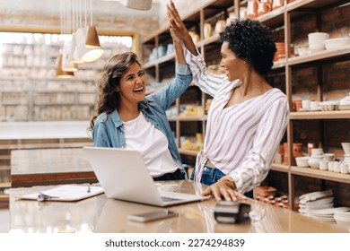 Ceramic shop owners high fiving each other while working in their store. Cheerful female ceramists celebrating their success as a team. Happy young businesswomen running a creative small business. - Powered by Shutterstock