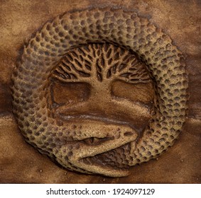 A Ceramic Snake Biting Its Tail With A Tree In The Middle.