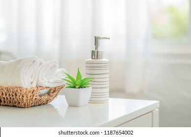 Ceramic soap, shampoo bottles and white cotton towels with green plant on white counter table inside a bright bathroom background - Shutterstock ID 1187654002