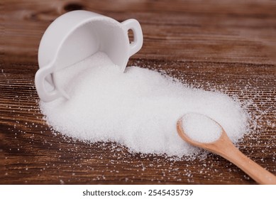 A ceramic sugar container tipped over, spilling sugar on a wooden table. A wooden spoon filled with sugar rests nearby, creating a rustic, natural scene - Powered by Shutterstock