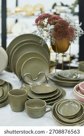 Ceramic tableware set including plates, bowls, cups and saucers arranged on table with decorative flowers in background, showcasing modern dining essentials for kitchen or restaurant