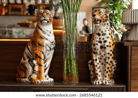 Ceramic tiger and leopard statues on wooden surface with glass vase. Decorative animal figurines for interior design, exotic style, and artistic home decor.
