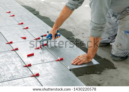 Ceramic Tiles. Tiler placing ceramic wall tile in position over adhesive with lash tile leveling system - Image