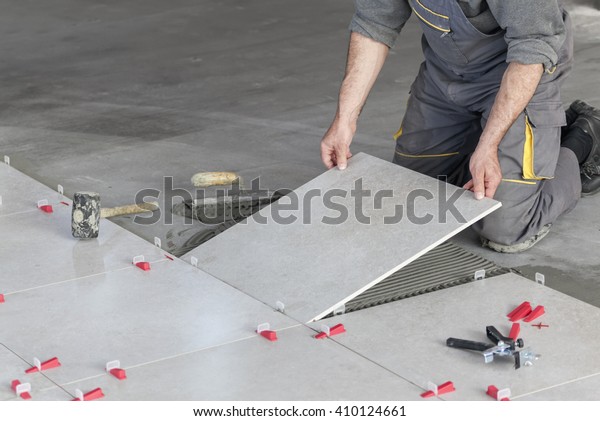 Ceramic Tiles. Tiler\
placing ceramic wall tile in position over adhesive with lash tile\
leveling system