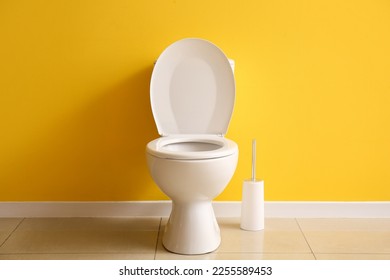 Ceramic toilet bowl and brush near yellow wall