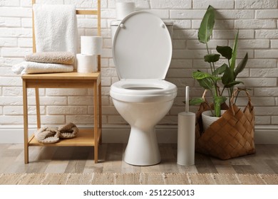 Ceramic toilet bowl and necessities near white brick wall in restroom