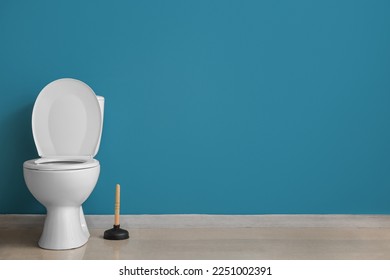 Ceramic toilet bowl and plunger near blue wall