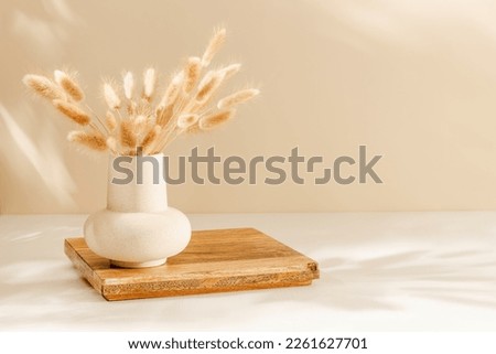 Ceramic vase with lagurus grass on the wooden stand with copy space for home product presentation, warm cozy sunlight and shadows. Scandinavian home interior decoration
