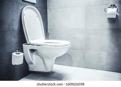 Ceramic white toilet bowl near grey wall, side light in the modern bathroom