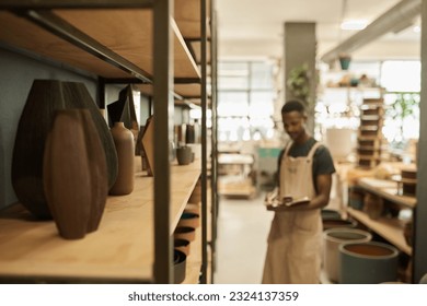 Ceramics sitting on workshop shelves with a potter in the background - Powered by Shutterstock