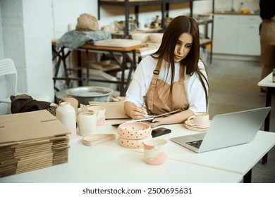 Ceramist with laptop working in studio, making notes - Powered by Shutterstock