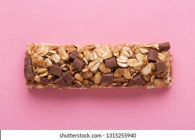 Cereal Bar Or Flapjack With Chocolate Chunks And Oat Flakes On Pink Background, Close Up