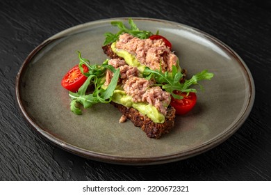 Cereal Bread With Tuna And Avocado In A Ceramic Plate On A Dark Textured Background. Restaurant Menu Isolated On Black