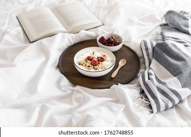 Cereal with cherries and yogurt in a white bowl on a round serving tray, white bedspread, an open book, striped blanket, healthy breakfast, bedroom
 - Powered by Shutterstock