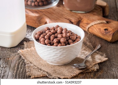 Cereal chocolate balls in bowl with milk on rustic wooden table