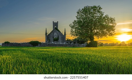 Cereal field illuminated by sunlight and old stone ruins of Ballinafagh Church with dramatic sky at sunset in background, County Kildare, Ireland - Powered by Shutterstock