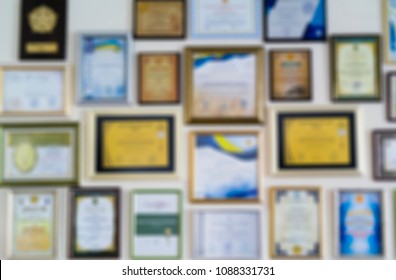 Certificates, diplomas and awards in frames on the wall. Abstract blurry background image.