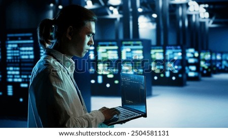 Certified asian technician running code on laptop, maintenancing and upgrading data center equipment designed to accommodate server rows, networking systems and storage arrays