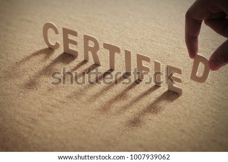 CERTIFIED wood word on compressed or corkboard with human's finger at D letter.
