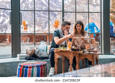 CERVO Hotel, Zermatt, Switzerland. March 15, 2022. Couple Enjoying Food While Sitting Against Window. Young Man And Woman Having Meal Together In Resort.