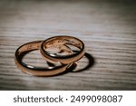 Cesis, Latvia - July 12, 2024 - Close-up of two intertwined gold wedding bands engraved with dates, placed on a wooden surface, casting soft shadows.