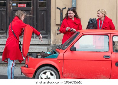 Cesis, Latvia - May 02, 2021: three women in red clothes at a red vintage car Fiat 126 with an open boot