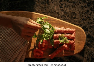 cevapi - fresh minced meat on wooden plate with tomatoes and parsley next to kitchen cloth with hand 