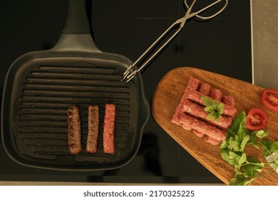 cevapi - fresh minced meat on wooden plate with tomatoes and parsley next to grill pan 