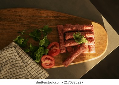 cevapi - fresh minced meat on wooden plate with tomatoes and parsley next to kitchen cloth 