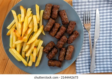 Cevapi, traditional balkan minced meat dish served with french fries in a navy blue plate on a wooden table