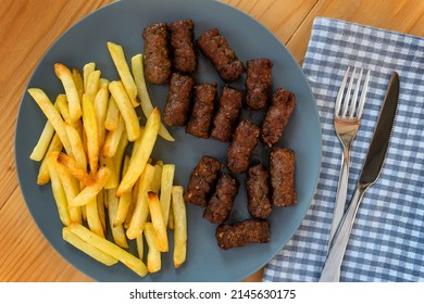 Cevapi, traditional balkan minced meat dish served with french fries in a navy blue plate on a wooden table