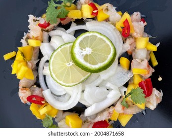 Ceviche From Fresh Shrimps With Mango, Onion And Lime Slices On A Black Plate Directly Above View