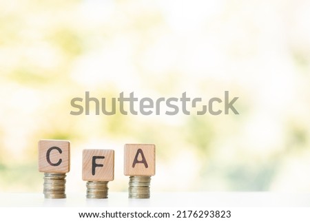 CFA word written on wood cubes, stacks of coins, nature green background.