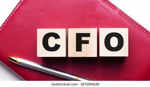 CFO is made up of wooden cubes that stand on a burgundy notebook near the pen. Business concept